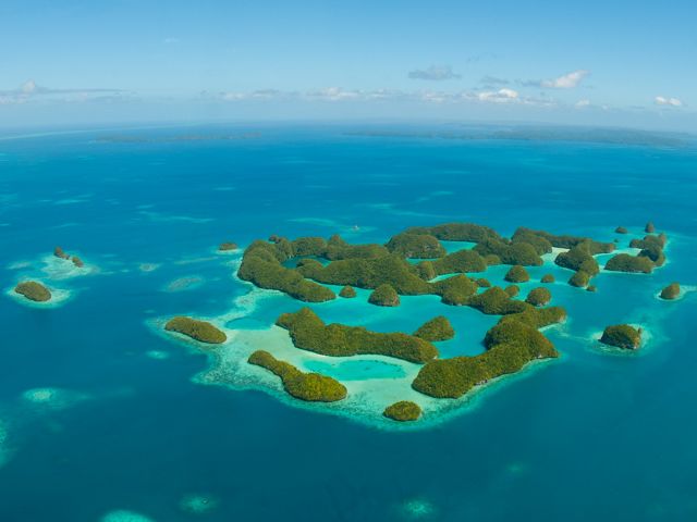 Aerial photo of tropical islands against a deep, blue sea, ringed by shallow coral reefs.
