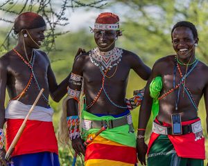 Three young men dressed in colorful beads laugh together.