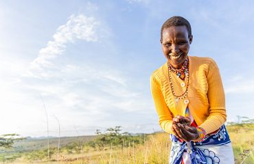 A woman wearing a yellow sweater holds a handful of seeds.