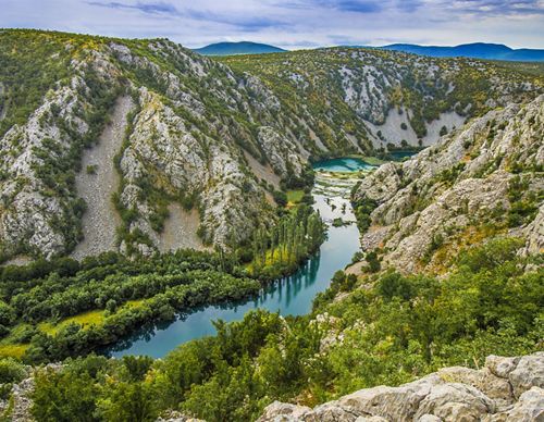 A canyon of the Krupa River that meanders through trees, plants and rocks.