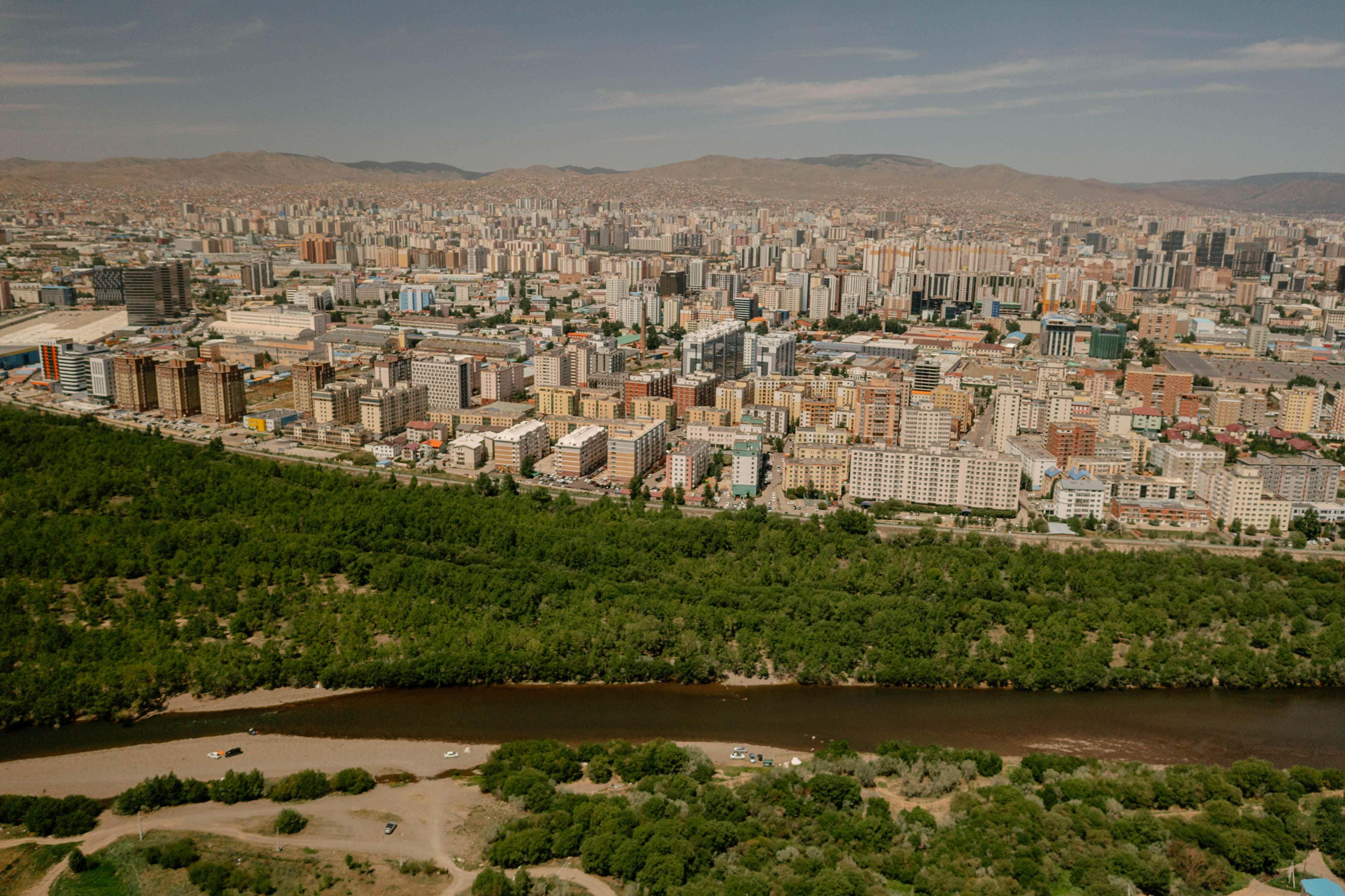 City buildings sit right next to forested area along river.