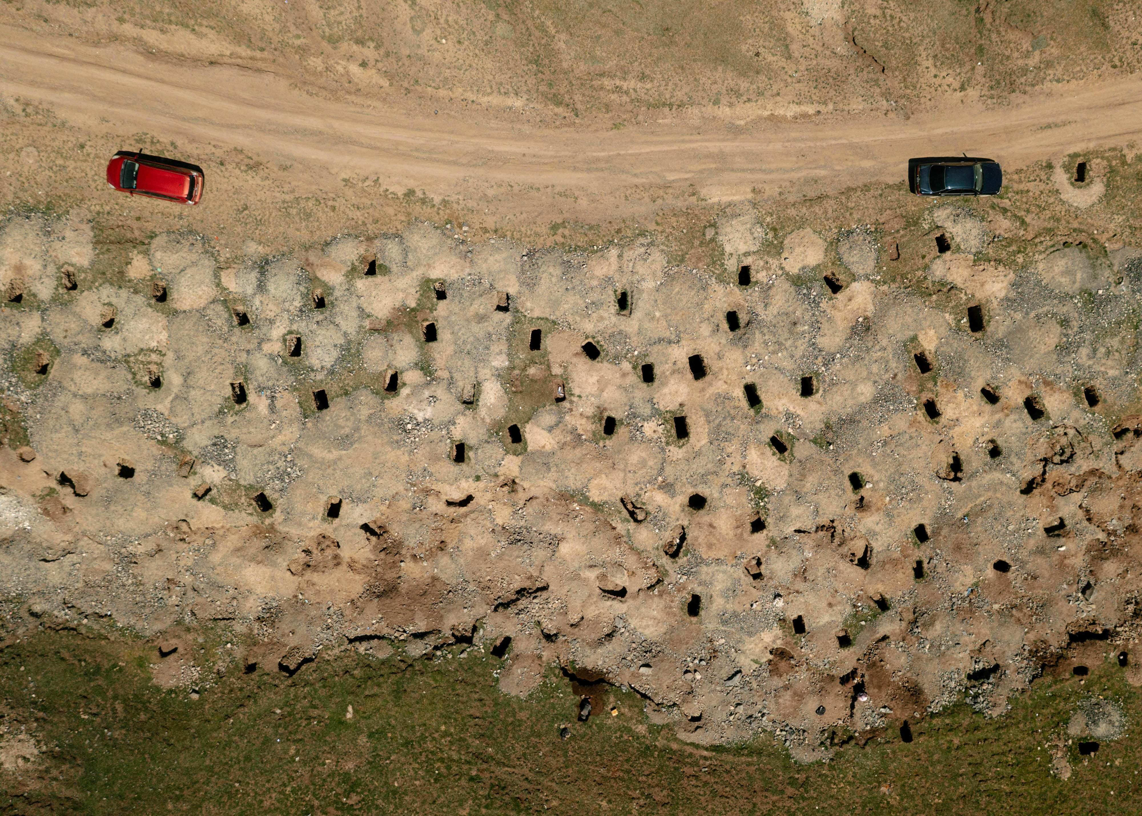A group of cars along an area of sand with many holes in it.