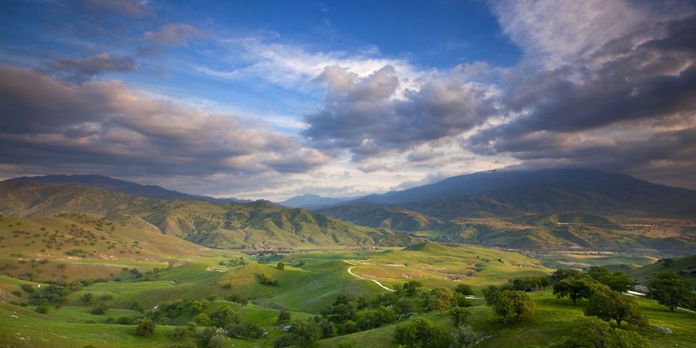 View looking across a wide valley with rolling green hills and mountains in the distance.