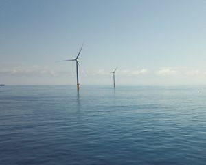 small boat on still sea with offshore wind turbines in distance.