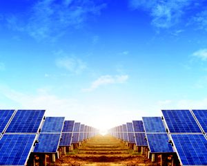 Looking between two large arrays of solar panels, blue sky above.