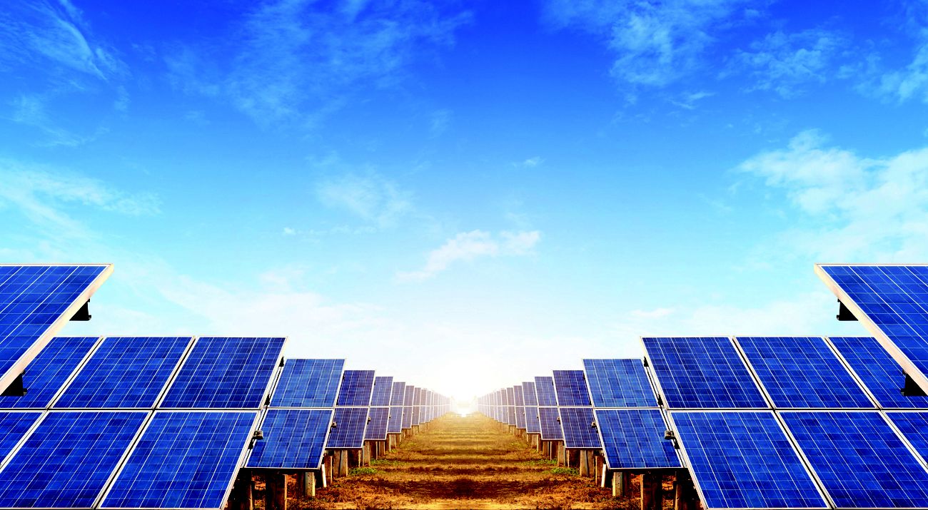 Looking between two large arrays of solar panels, blue sky above.