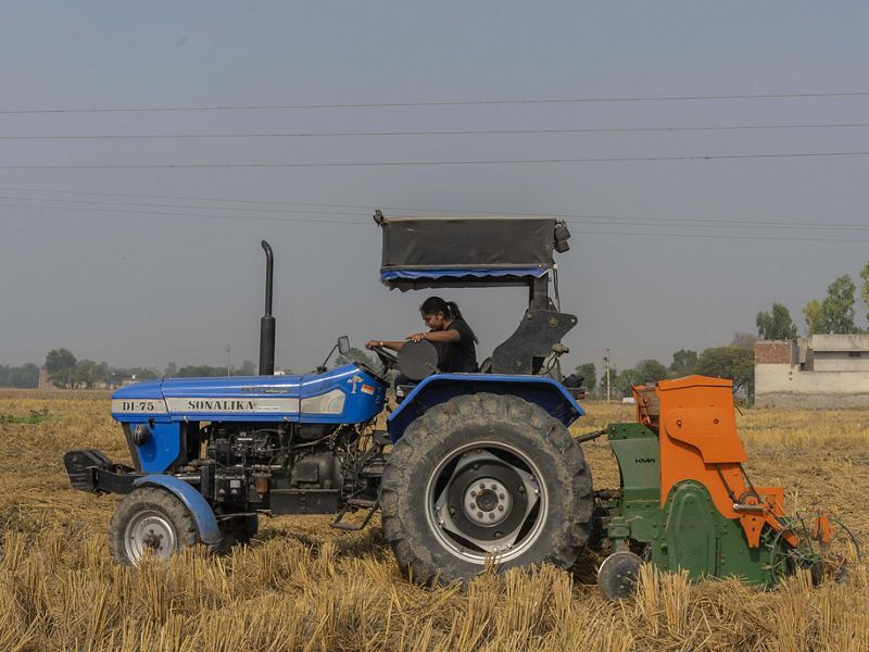 Amandeep drives through a dry rice field with a blue tractor with an orange attachment in back known as the super seeder. 