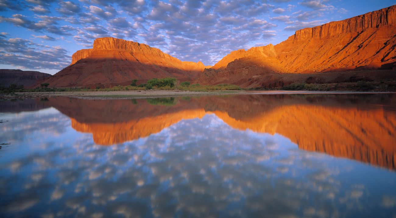 a calm river with red rock mountains in the background.