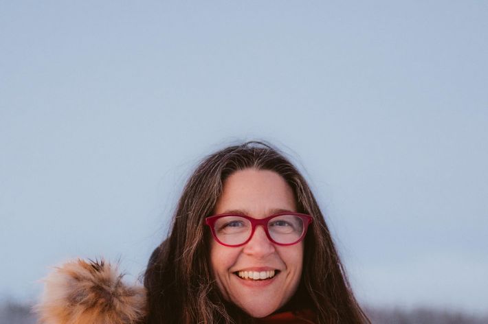 tracey williams woman stands outside near frozen lake with red parka